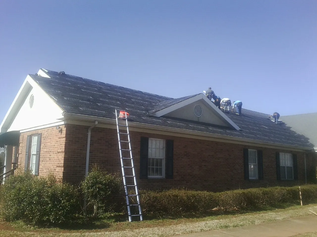 Crew tearing shingles off a brick ranch roof with a ladder set — Metal Roof Repair work by our crew in Stockton