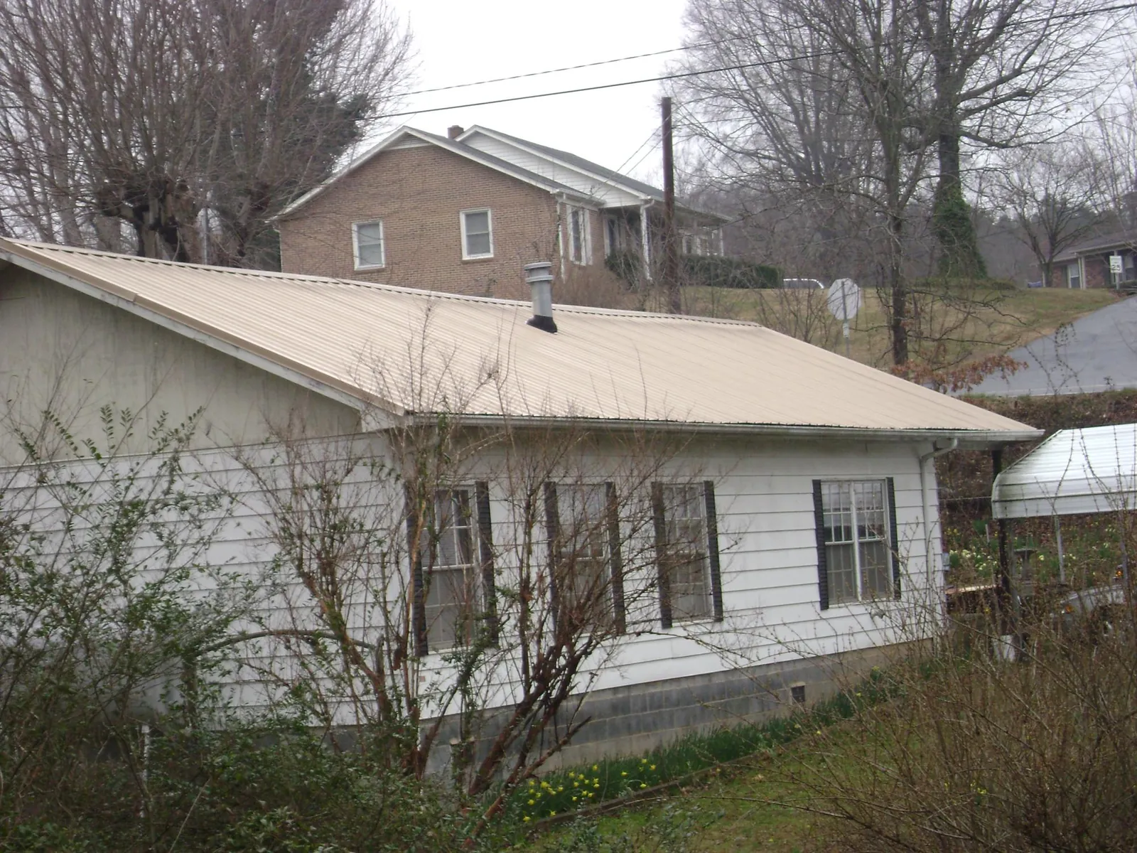 Tan metal roof on a white sided house set into a hillside — Commercial Roofing by Roofing Brothers in Stockton